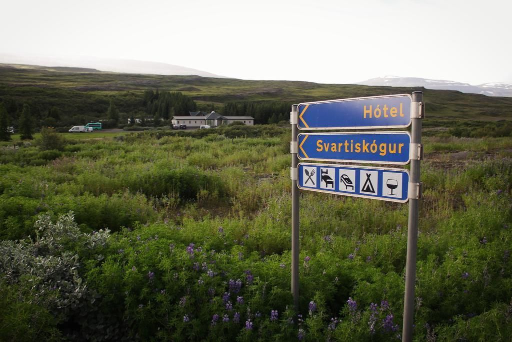 A signpost with directions to 'Hotel' and 'Svatiskógur' with symbols indicating amenities like a bed, toilet, and picnic area.