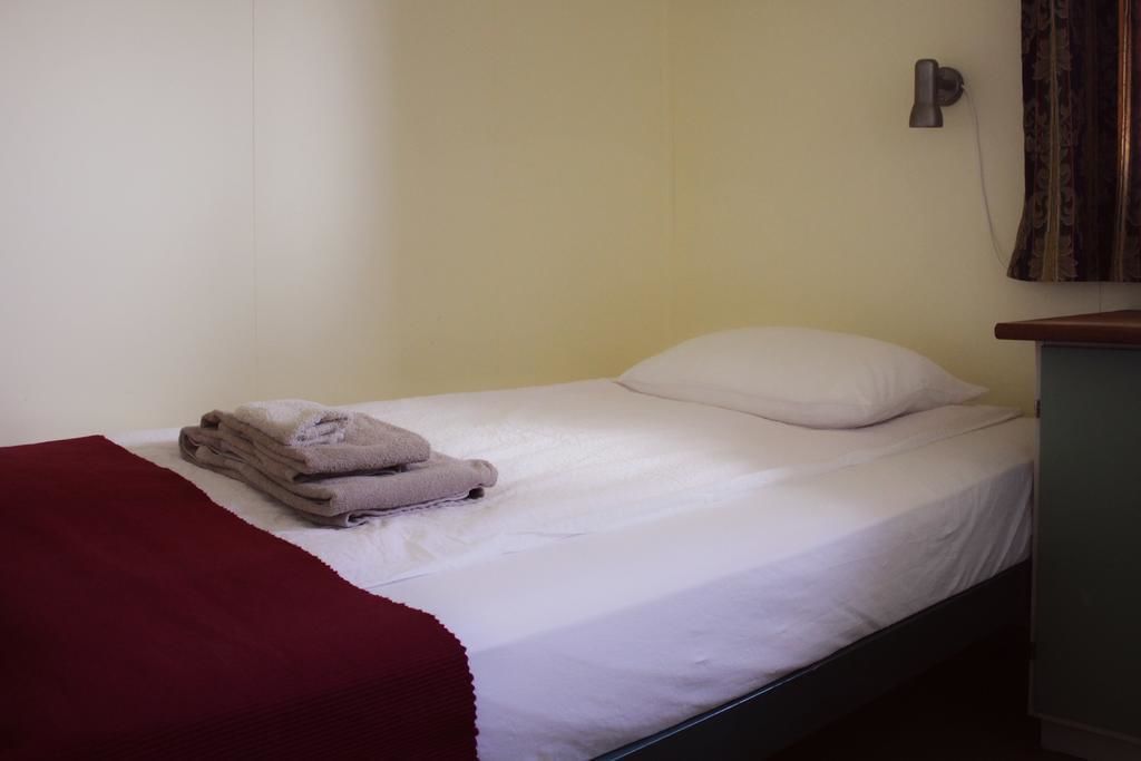 Un lit simple avec une literie blanche, une couverture rouge et une serviette pliée posée sur le côté.