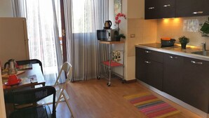 A compact kitchen with dark cabinets, a microwave, a kettle, and a small dining area with a table and chairs. - Bnbook Passirana Studio with fast wifi (RHO)