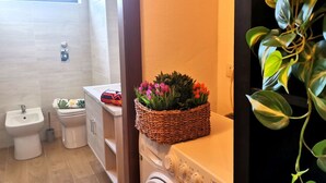 A bathroom with a washing machine, a bidet, and a toilet. There is a basket of flowers on the washing machine. - Bnbook Passirana Studio with fast wifi (RHO)