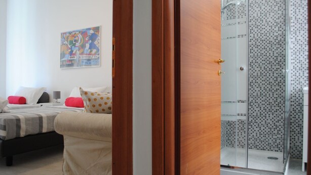 Une chambre à coucher comprenant un lit, des oreillers, une table de chevet et un espace douche doté d’une porte en verre.