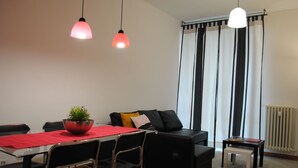 Un salon moderne avec une table à manger, un canapé en cuir noir et deux lampes suspendues.