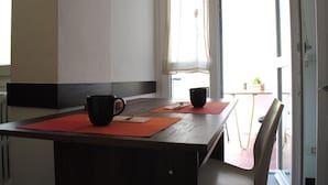 Un coin repas avec une table en bois, deux tasses noires et des sets de table rouges.