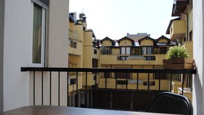 Un balcon doté d’une table et de chaises en bois, d’où l’on peut admirer une rangée de bâtiments jaunes, eux aussi pourvus de balcons.