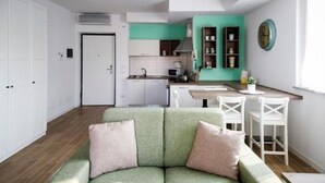 A modern living room with a green sofa, a kitchen in the background, and a dining area with white chairs. - Bnbook Don Sturzo with super wi fi (Cornaredo)