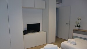 A modern hotel room with a bed, a TV on a white cabinet, a potted orchid, and neatly folded towels. - Bnbook Don Sturzo with super wi fi (Cornaredo)