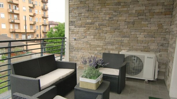 A balcony with wicker furniture, a potted plant, and an air conditioning unit. - Bnbook Don Sturzo with super wi fi (Cornaredo)