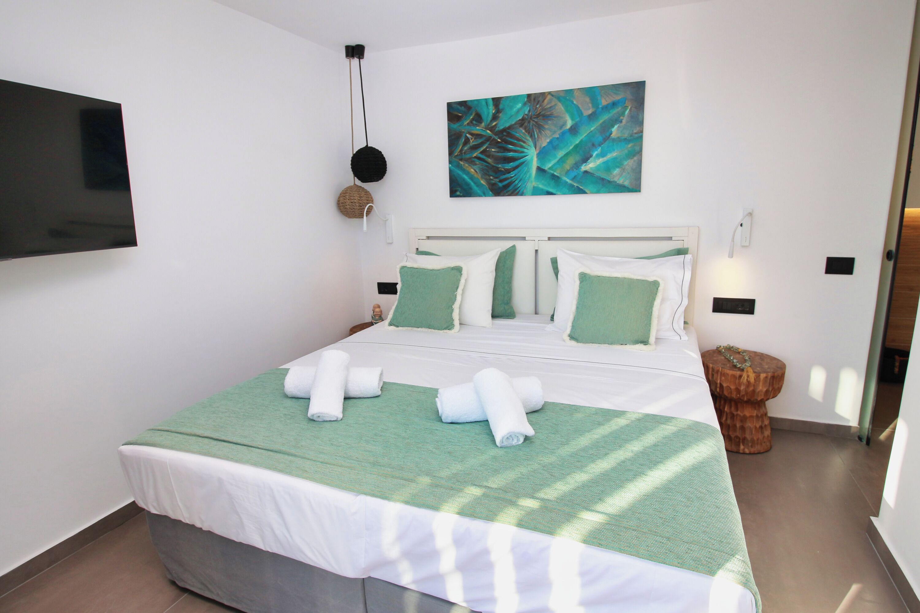 A neatly made bed with green and white bedding, a wall-mounted TV, and a painting above the bed.