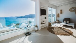 A modern living room with a large window overlooking a coastal view, a white sofa, a small coffee table, and decorative items.