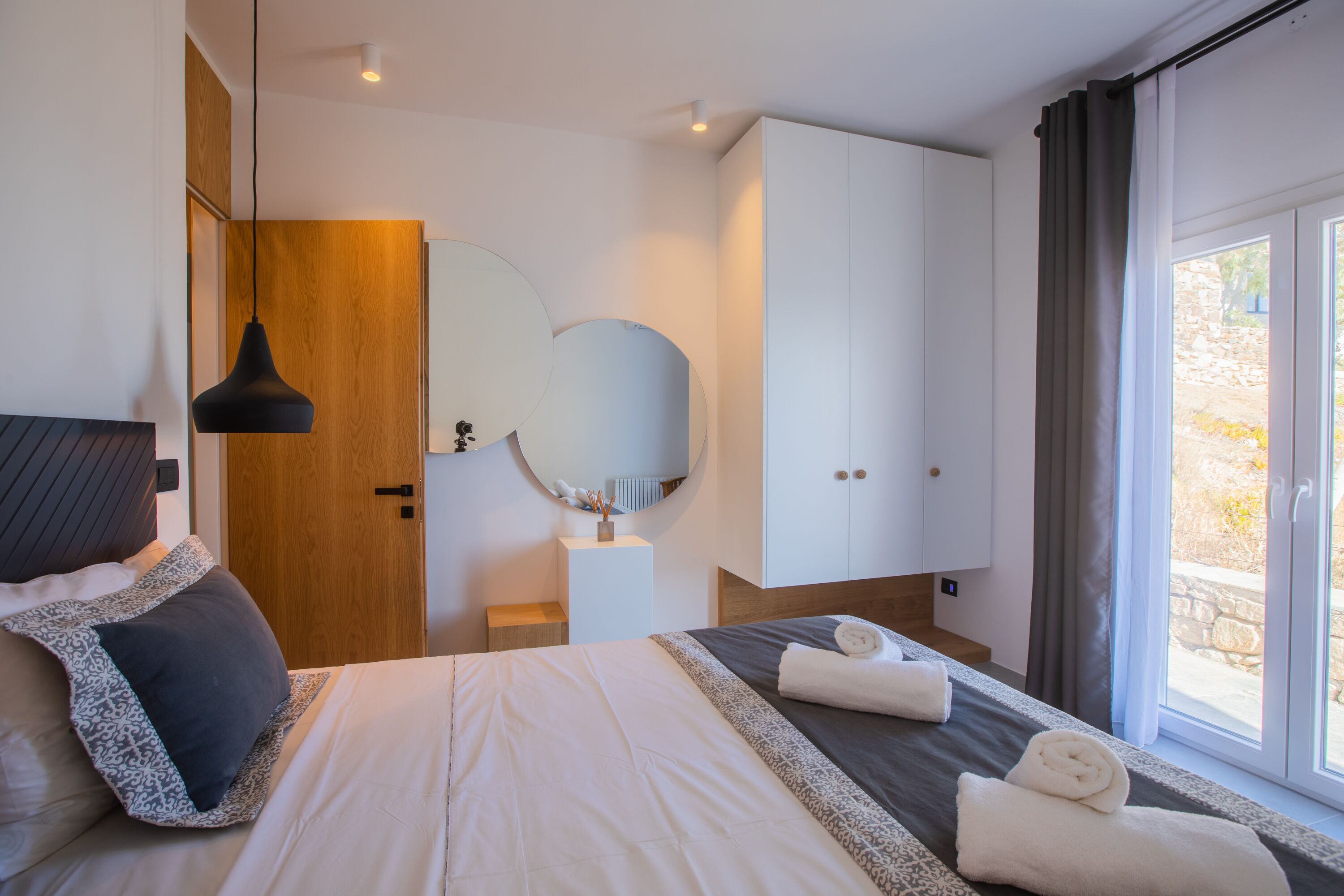 A modern bedroom with a large bed, a bedside table, a mirror, and a wardrobe.