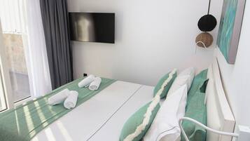 Una cama bien hecha con ropa de cama blanca y verde, un televisor de pantalla plana en la pared y una ventana con cortinas.