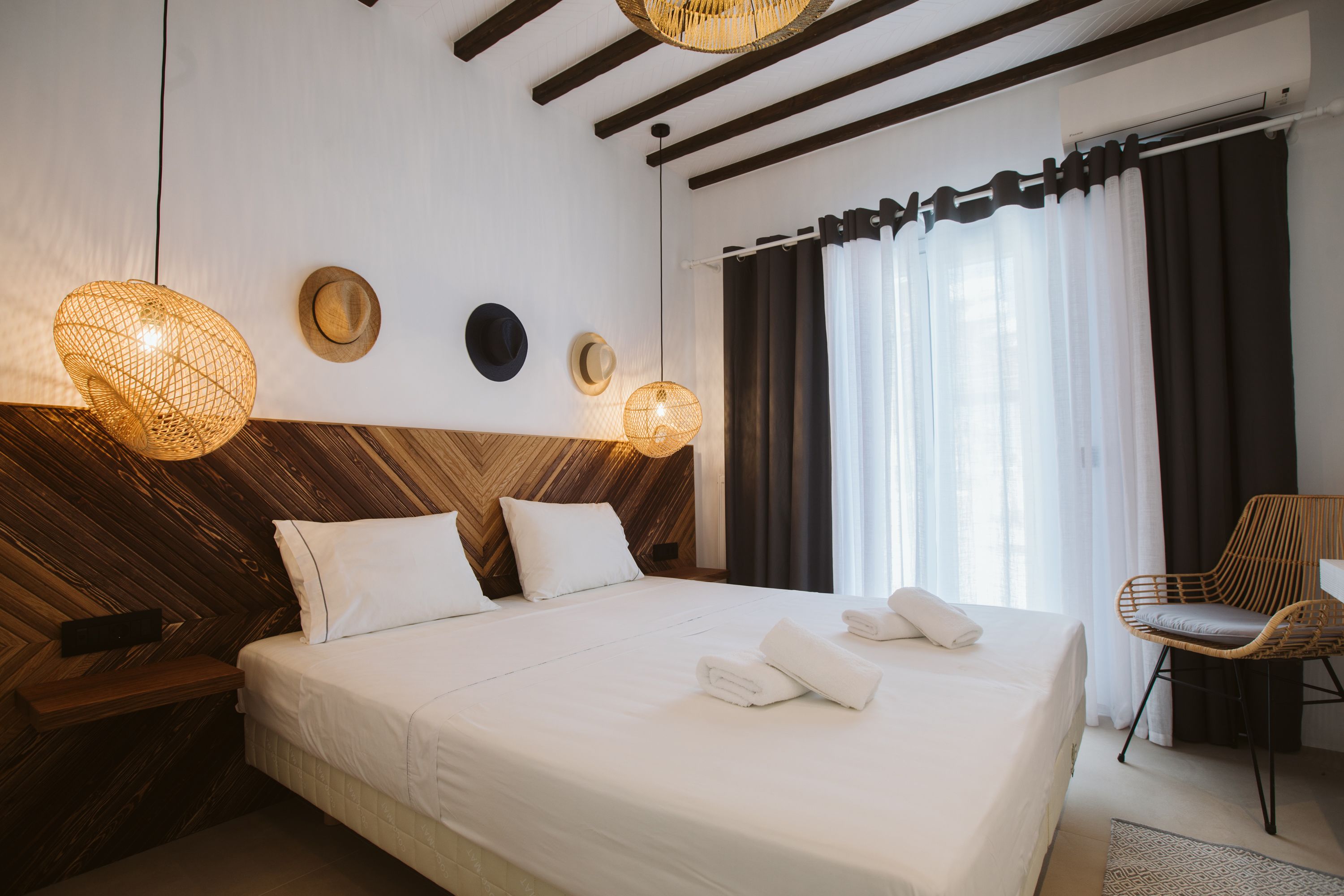 A hotel room with a large bed, wooden headboard, two wall-mounted lamps, a chair, and a window with curtains.