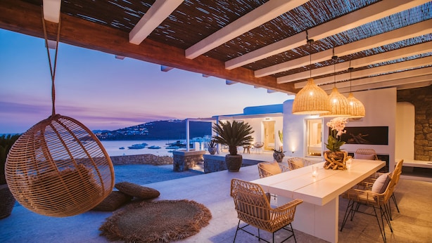 An outdoor dining area with a view of the sea, a hanging chair, and a stone wall.