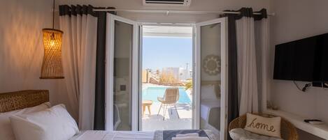 A hotel room with a bed, a chair with a pillow labeled "home," an air conditioning unit, and a view of an outdoor swimming pool.