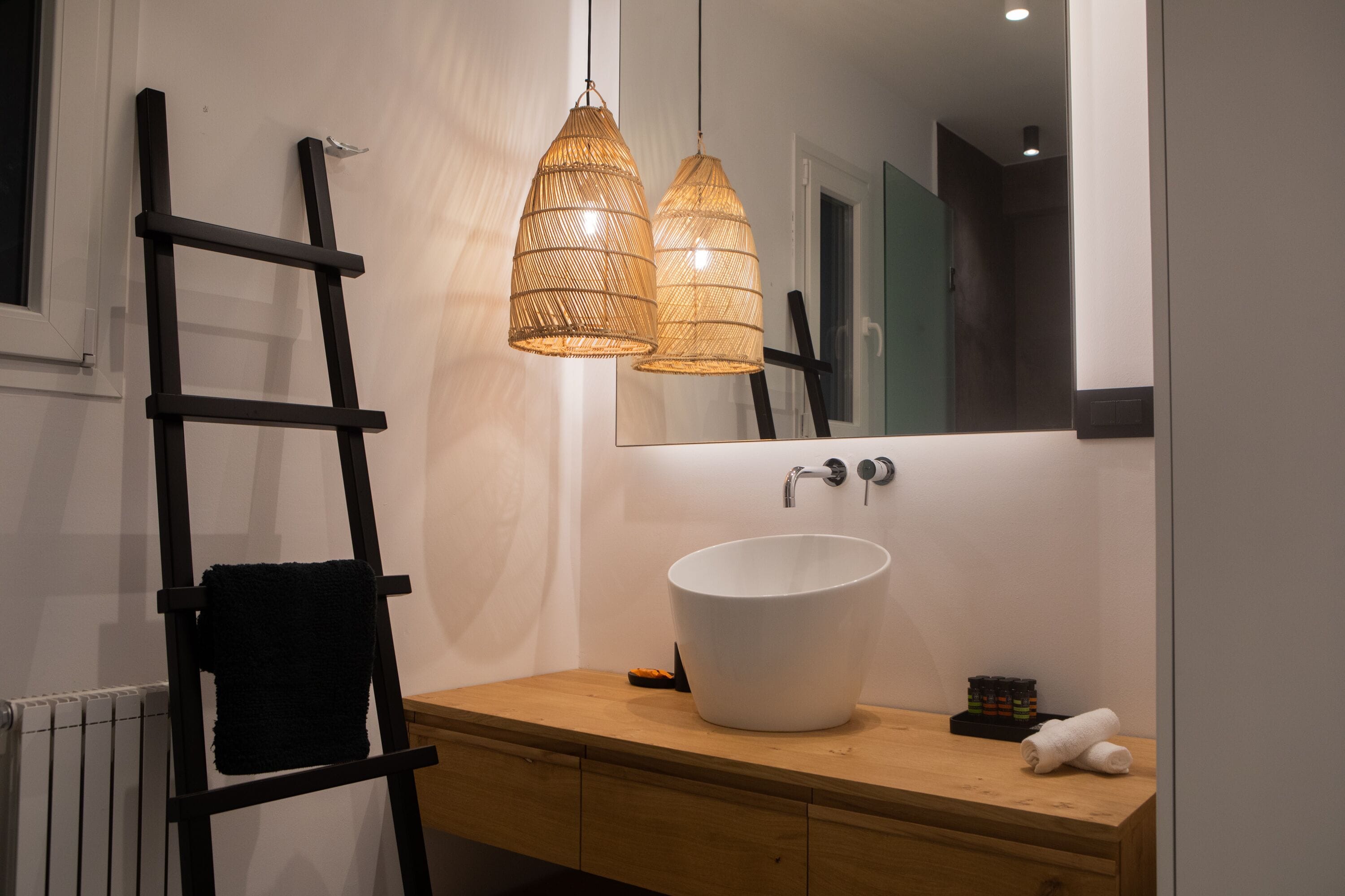 Ein Badezimmer mit einem Holzbadezimmerhocker, einem weißen Waschbecken und zwei hängenden Korbstuhnlampen.