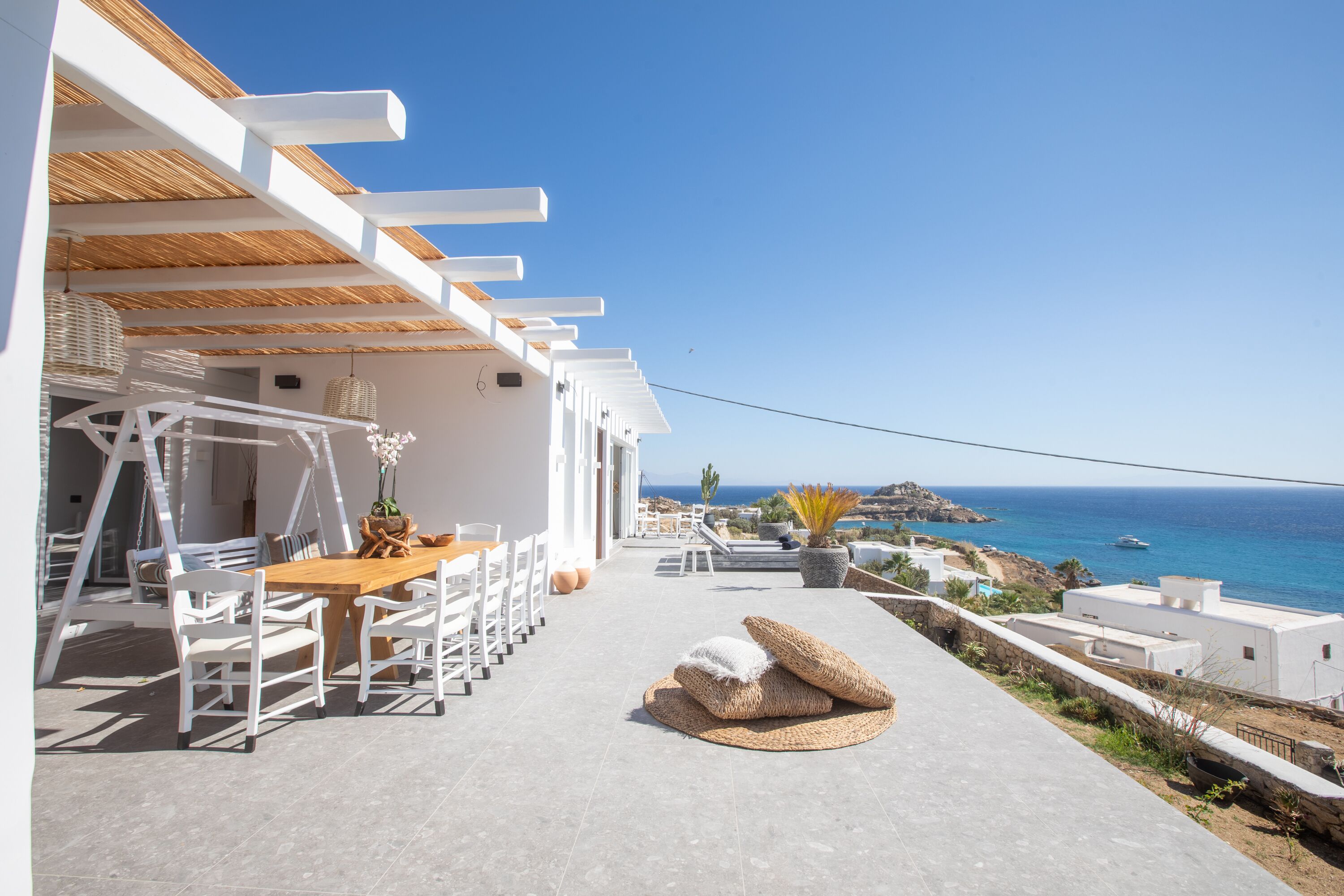 A terrace with a dining table and chairs, a wicker sofa, and a view of the sea.