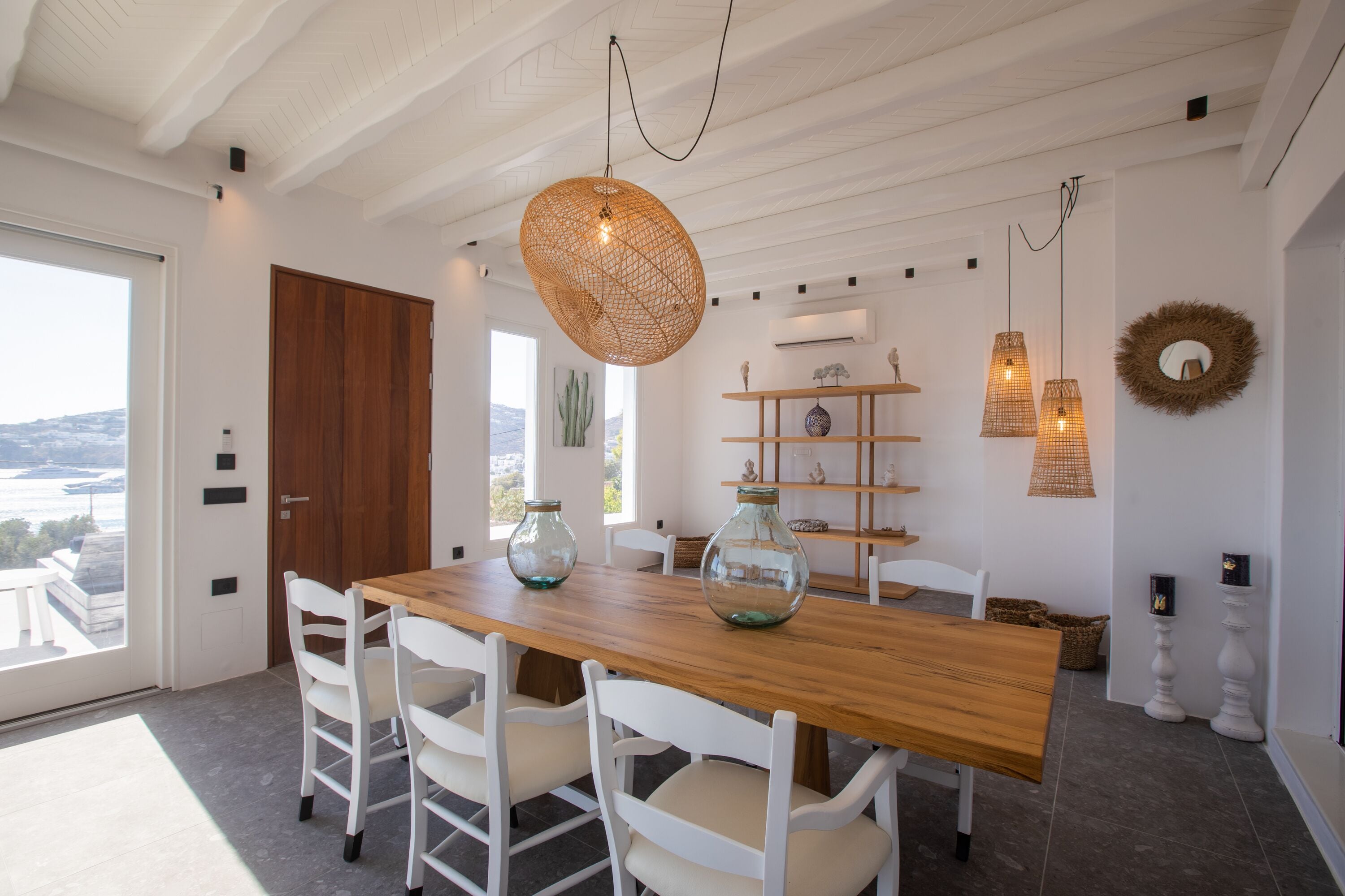 Un coin repas avec une table en bois, des chaises blanches et des lampes en osier suspendues au plafond.