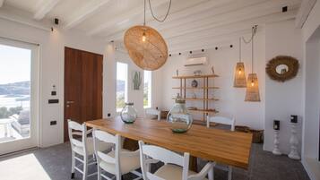 Un coin repas avec une table en bois, des chaises blanches et des lampes en osier suspendues au plafond.