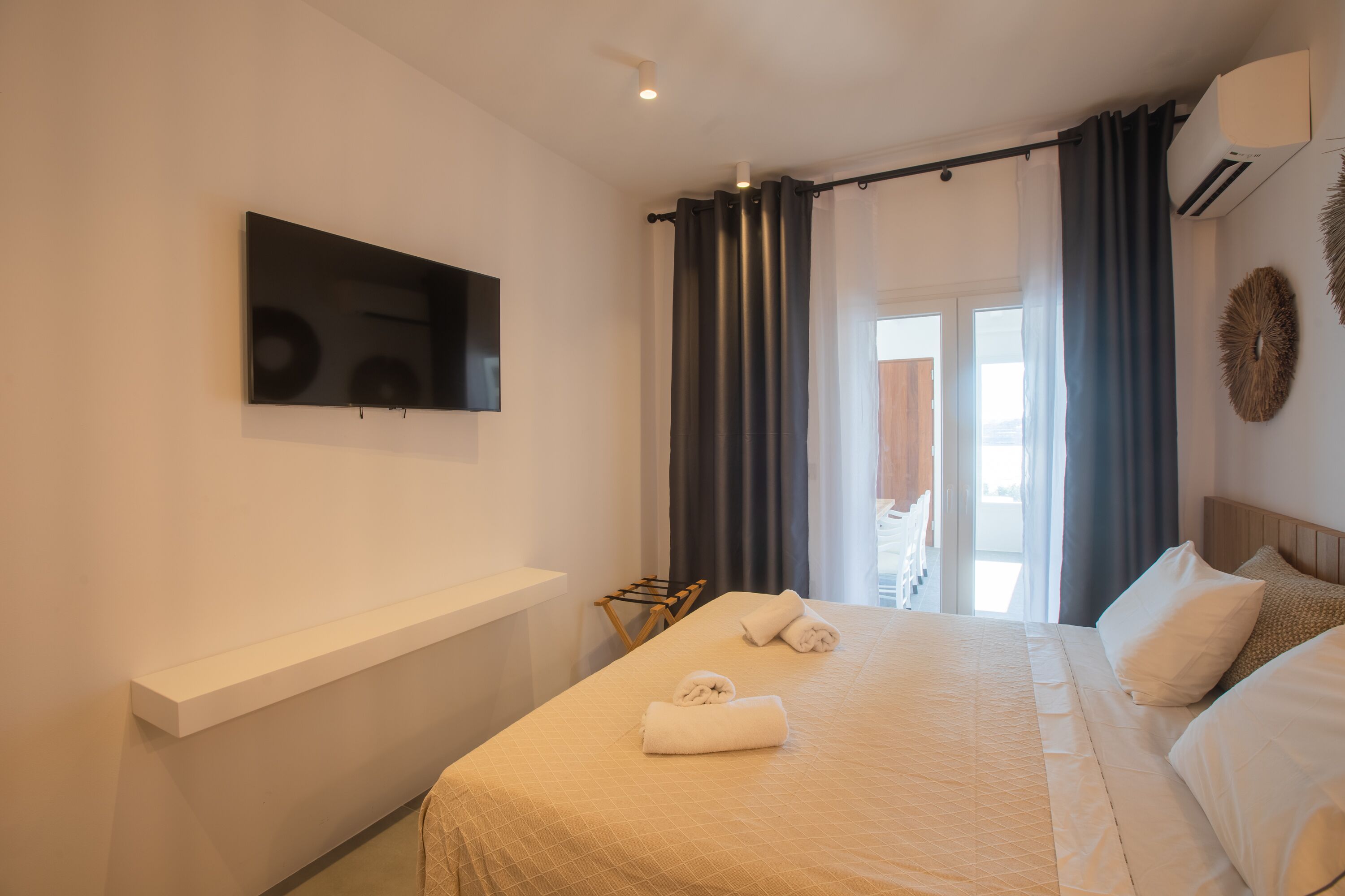Una habitación de hotel moderna con una cama grande, un televisor de pantalla plana en la pared, un pequeño rincón de descanso y vistas al exterior.