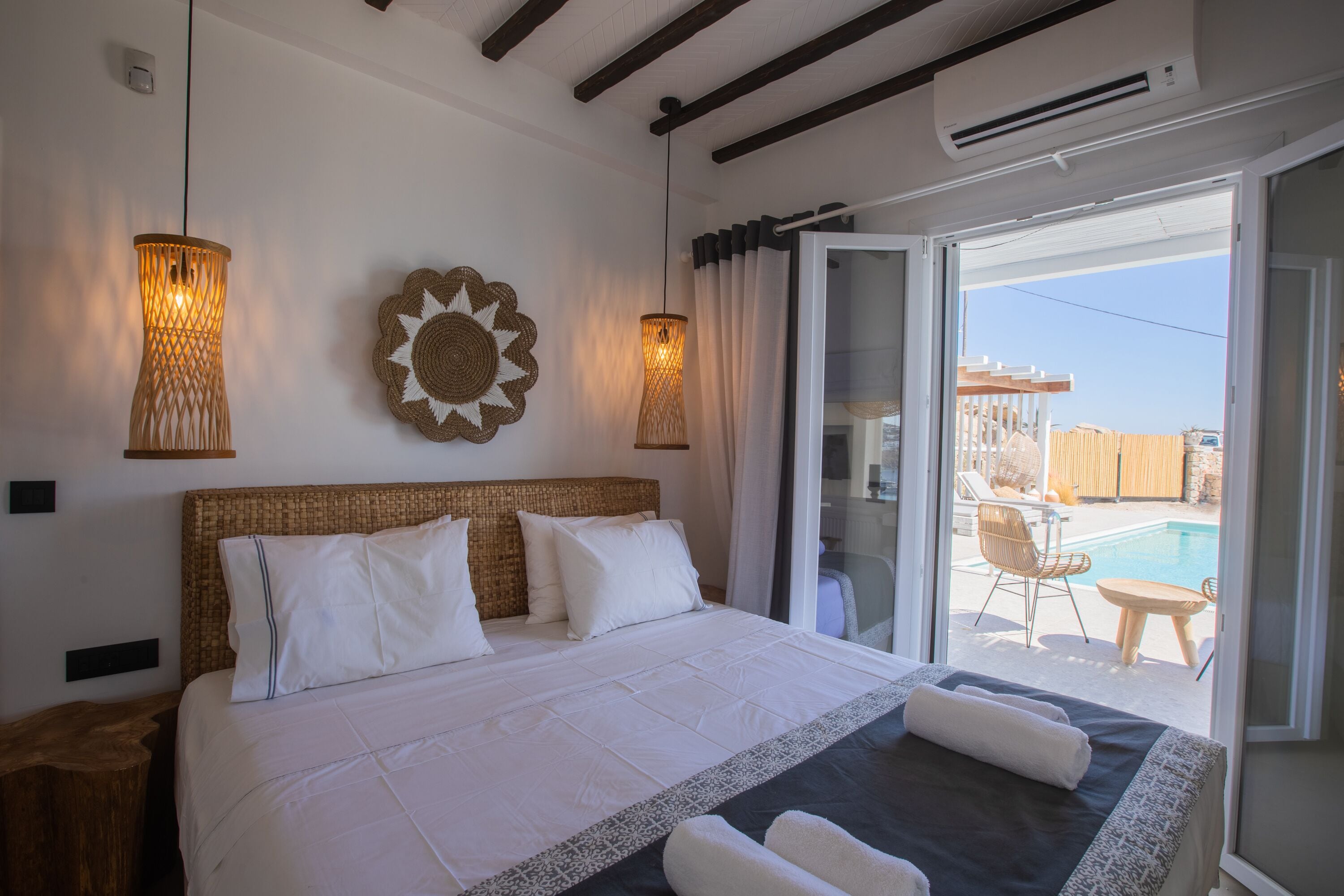 A hotel room with a large bed, a view of a swimming pool, and a balcony with outdoor furniture.