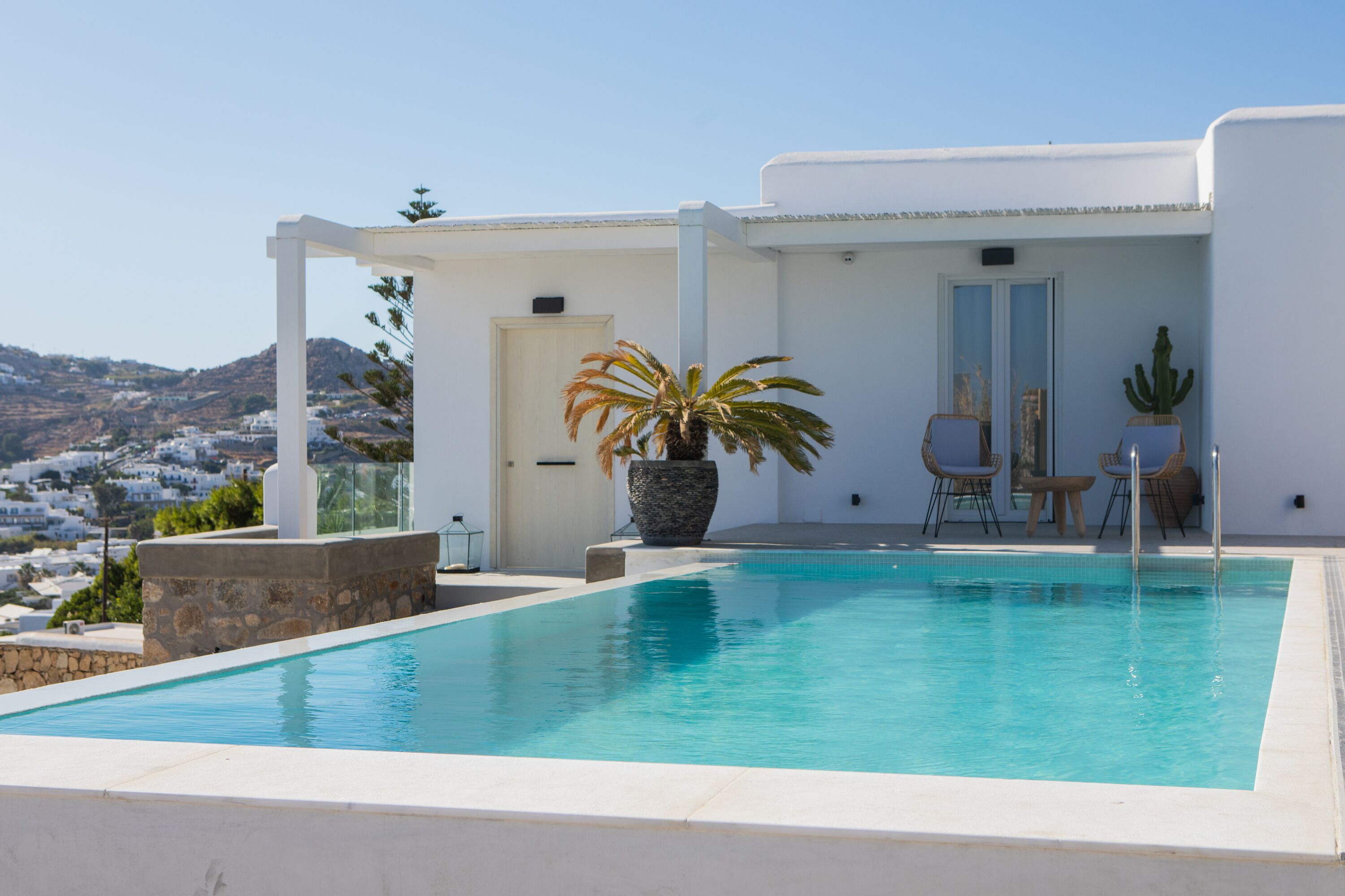 A pool area with a clear view of the surrounding landscape, a white building with a door, and a potted plant.