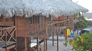 Uma estrutura de madeira com telhado de palha, deck de madeira e um pequeno espaço de estar ao ar livre.