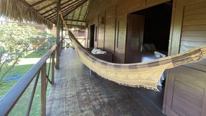Varanda de madeira com uma rede, cama com almofadas e vista para o exterior.