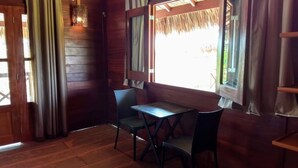 Interior de madeira com uma mesa, duas cadeiras, uma janela com vista e um candeeiro pendente.