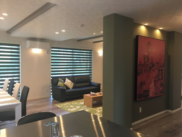 A modern living room with a dining area, a black leather sofa, and a large painting on the wall. - Casa Verde Hakuba (Hakuba)