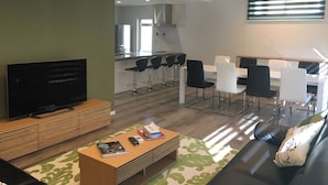 Una sala de estar moderna con un televisor de pantalla plana, un sofá, una mesa de centro y un comedor con sillas y una mesa.
