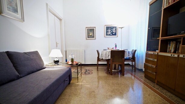Una sala de estar con sofá, una mesa de centro, una mesa de comedor con sillas, una estantería y cuadros enmarcados en la pared.