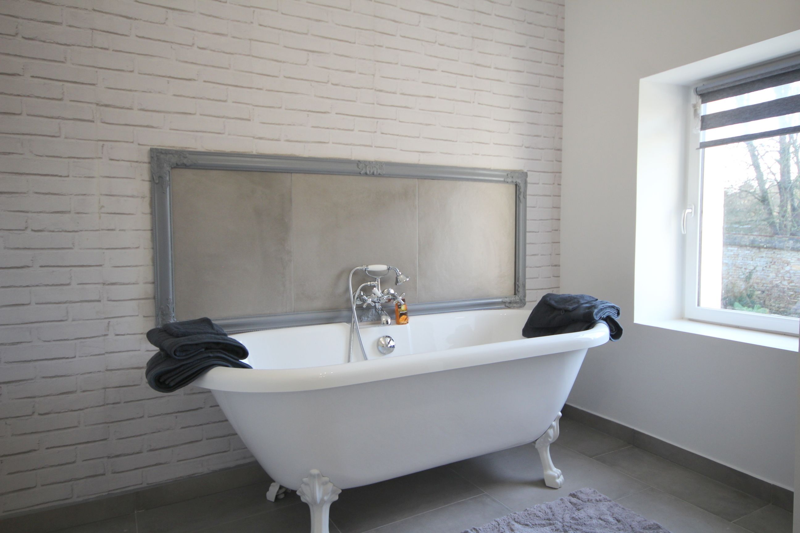 A bathroom with a white bathtub, a window, and a brick wall.