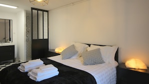 Een moderne slaapkamer met een groot bed, zwart-wit beddengoed, een zwart hoofdeinde, een nachtkastje met een lamp en een spiegel boven de dressoir.