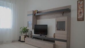 Un salon moderne avec un téléviseur à écran plat, un meuble de rangement en bois et une plante en pot.