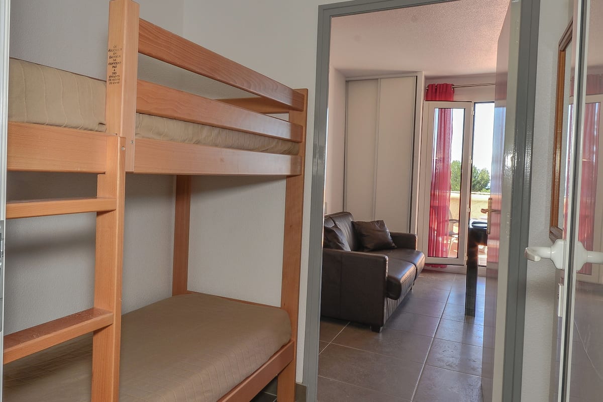 A room with a bunk bed, a sofa, and a sliding glass door leading to an outdoor area.