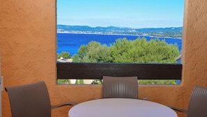 A balcony with a white table and two chairs, overlooking a coastal view with trees and distant land. - VVF Résidence Saint-Cyr-sur-Mer (Saint-Cyr-sur-Mer)