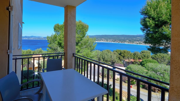 A balcony with a table and chairs, overlooking a coastal view with trees and a clear sky. - VVF Résidence Saint-Cyr-sur-Mer (Saint-Cyr-sur-Mer)