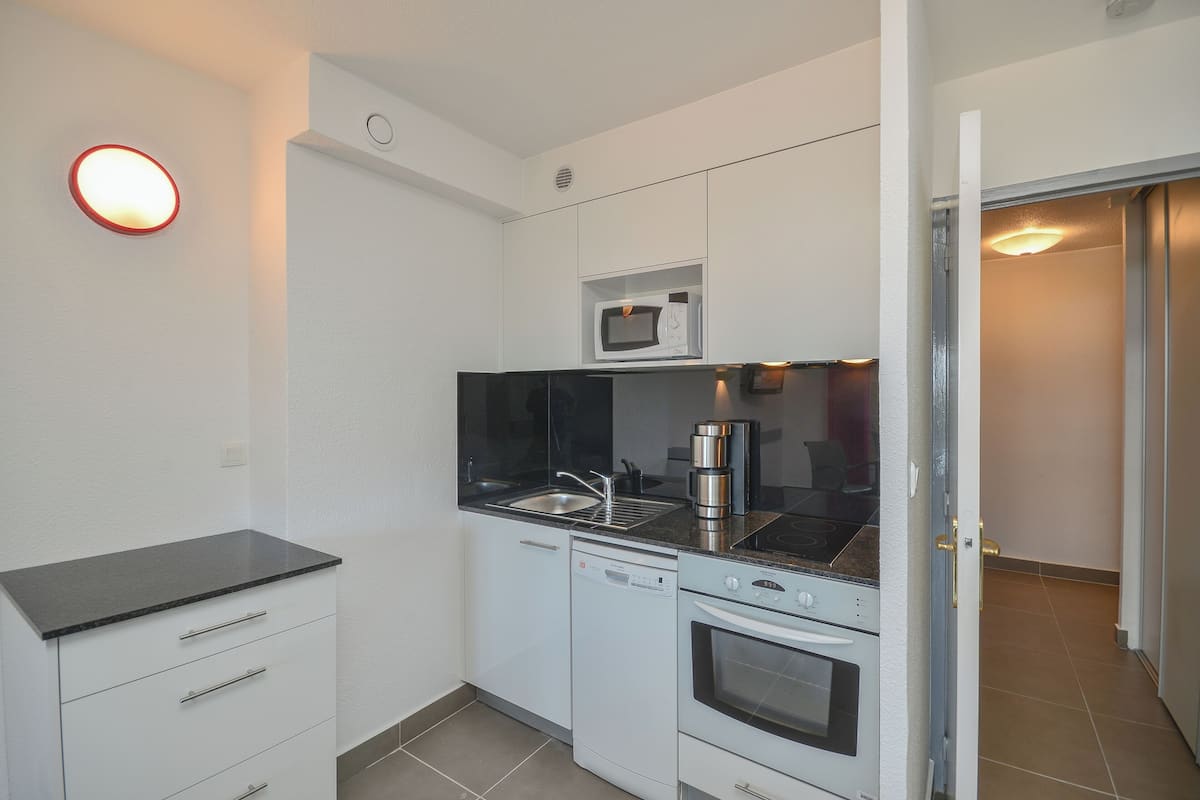 A compact kitchen with white cabinets, a black countertop, a built-in microwave, a coffee maker, and a dishwasher.