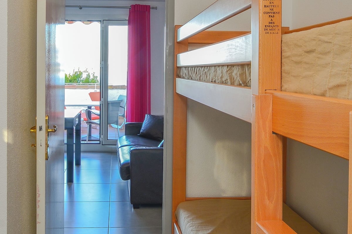 A room with a bunk bed, a sofa, and a sliding glass door leading to an outdoor area with a table and chairs.