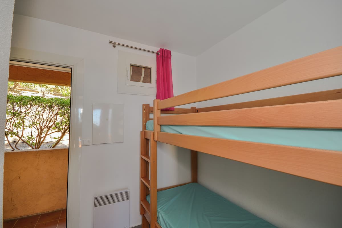 A bunk bed room with a window, a radiator, and a small window above the bed.