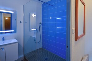 Ein modernes Badezimmer mit Duschkabine aus Glas, einem weißen Waschbecken und einem Spiegel mit blauer Beleuchtung.