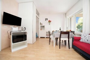 A modern living room with a flat-screen TV, a dining table with chairs, a sofa, and a kitchen area with a microwave. - Riva Lago e Spiaggia Apartment with Balcony and Parking, Riva del Garda, Italy (Riva del Garda)