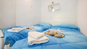Ein Hotelzimmer mit blauer Bettdecke, einer weißen Wand, einem Regal mit Dekoration und einem Tablett mit Teekanne und Tassen.