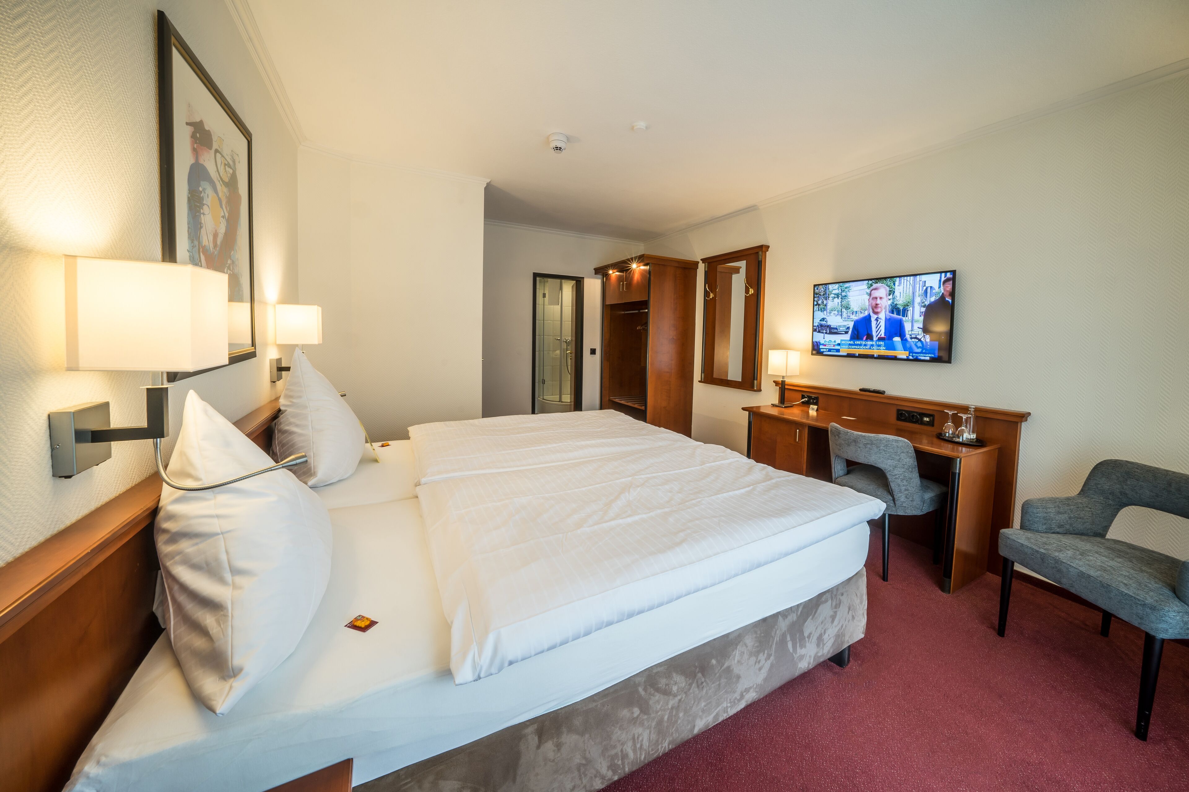 A hotel room with a bed, bedside lamps, a desk with a chair, a television, and a mirror.