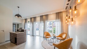 A modern hotel lobby with a reception desk, two leather chairs, a coffee table, and a large window with curtains. - Hotel Meyerink (Vreden)