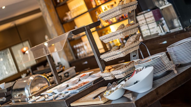 A buffet setup with wicker baskets and plates, a glass display case, and a wooden counter. - Hotel Meyerink (Vreden)