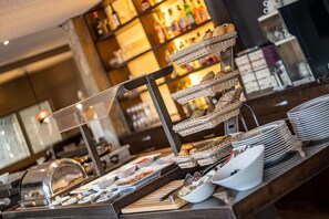 A buffet setup with wicker baskets and plates, a glass display case, and a wooden counter. - Hotel Meyerink (Vreden)
