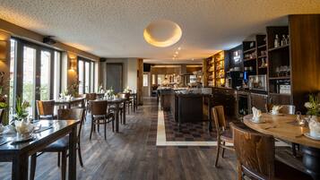 A spacious hotel lobby with a central bar area, wooden flooring, and large windows providing natural light.