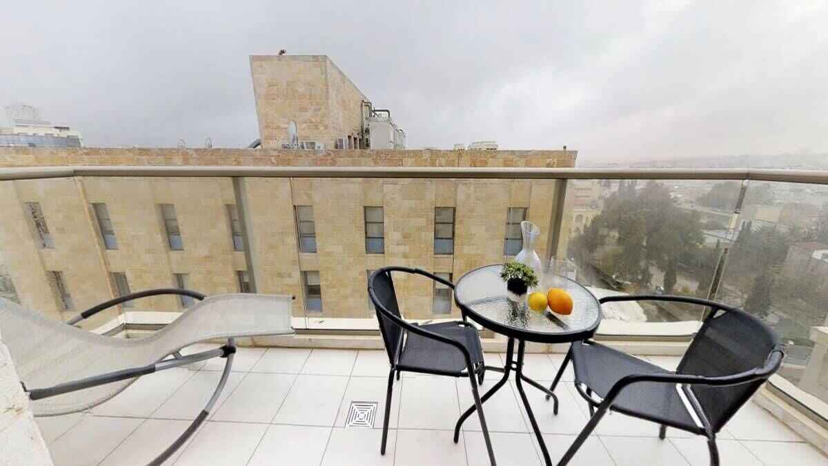 A balcony with a table and chairs, a vase with flowers, and a view of buildings.