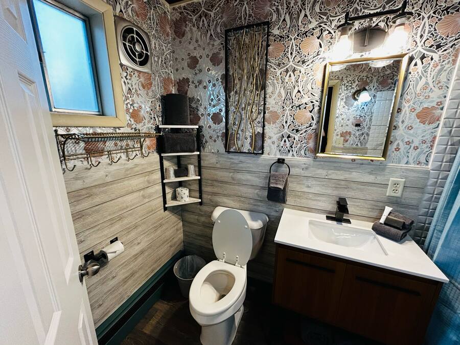 Un bany amb terra de fusta, un vàter, un lavabo, un mirall i una barra per a tovalloles.